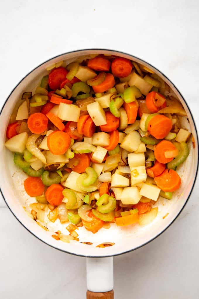potatoes, carrots and celery sautéing in a white pot