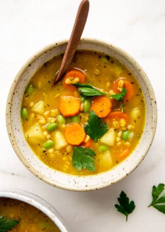vegetable barley soup in a speckled bowl with a wood spoon