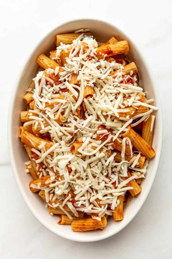 ziti noodles in sauce topped with shredded cheese in a baking dish