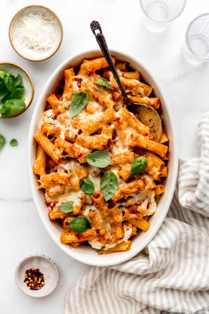 Baked ziti in an oval dish with a striped napkin on the side