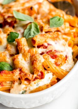 A close up of baked ziti topped with cheese and basil leaves