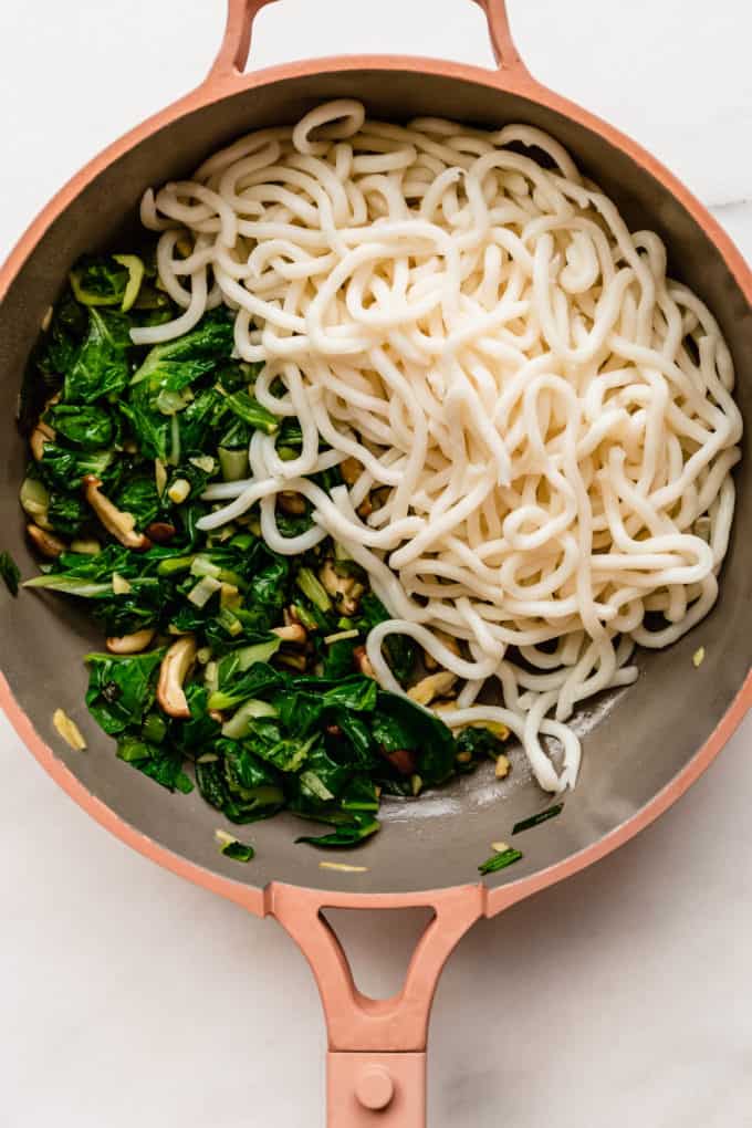 udon noodles and sautéed bok choy in a pink pan