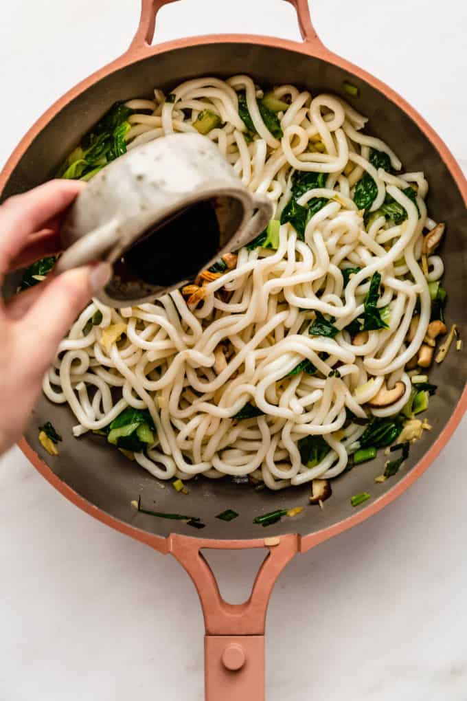 Stir fry sauce being poured into a pan of udon noodles