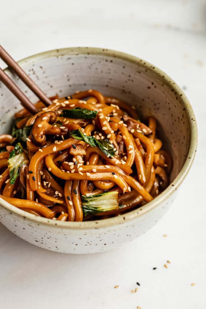 Yaki udon in a speckled ceramic bowl with wood chopsticks in it