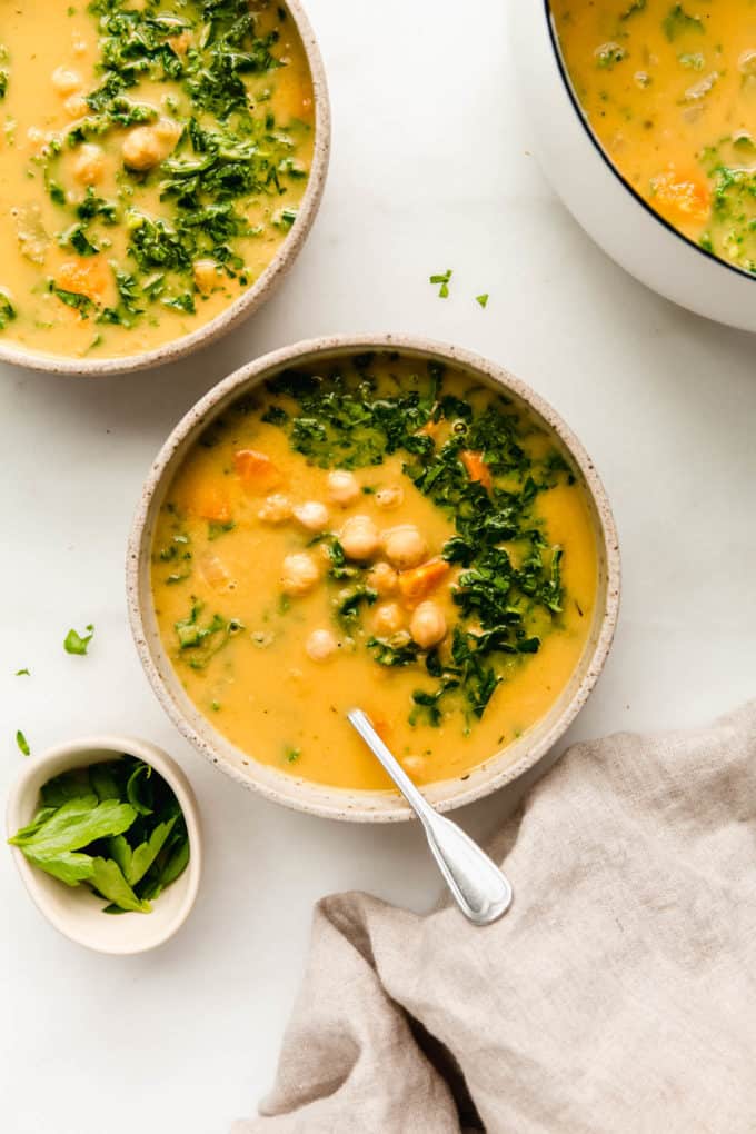 Two bowls of chickpea soup with a side of parsley