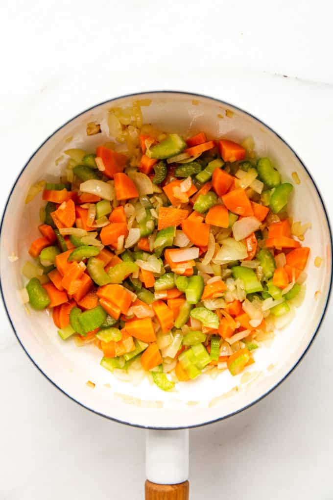 a white pot with chopped carrots, celery and onions in it