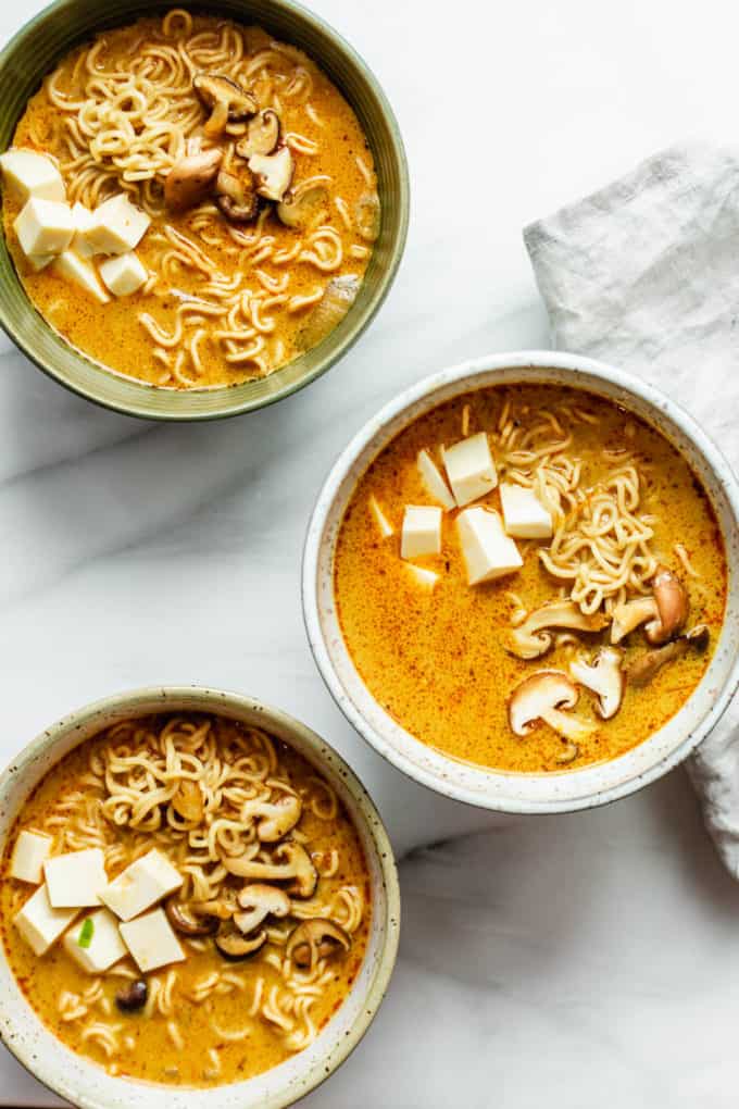 three bowls of coconut curry ramen with shitake and tofu in them