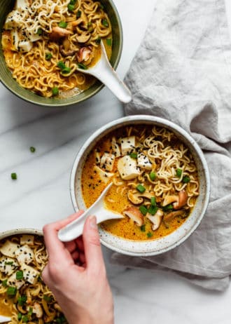 A hand scooping a spoon out of a bowl of coconut curry ramen