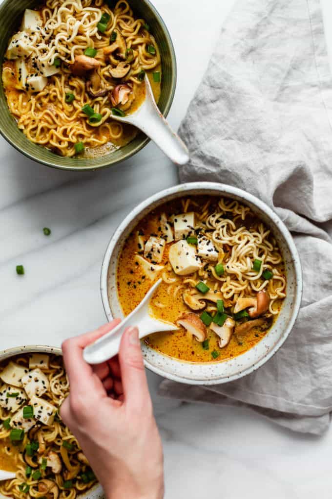 A hand scooping a spoon out of a bowl of coconut curry ramen