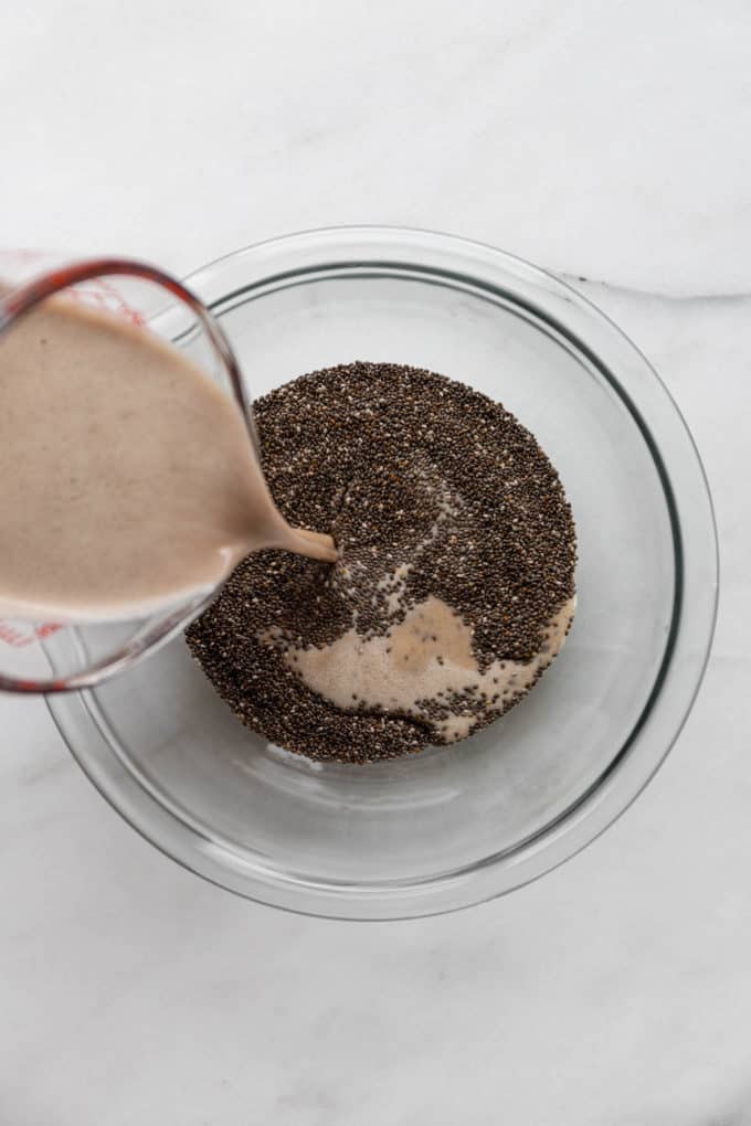 a measuring cup pouring eggnog into a bowl of chia seeds
