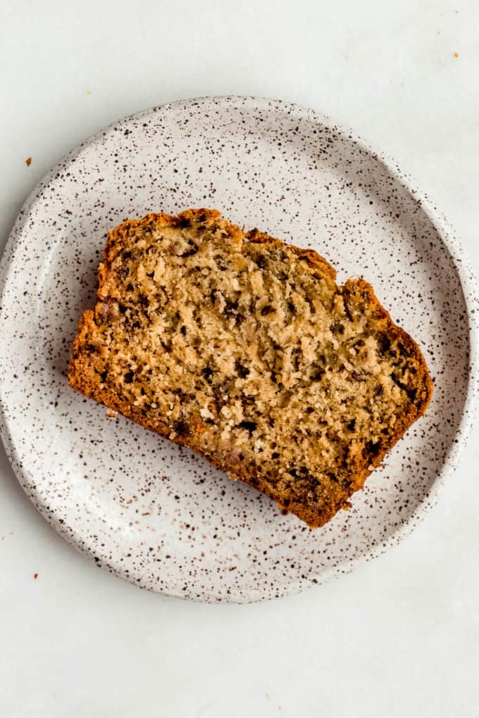 a slice of vegan banana bread on a white speckled plate