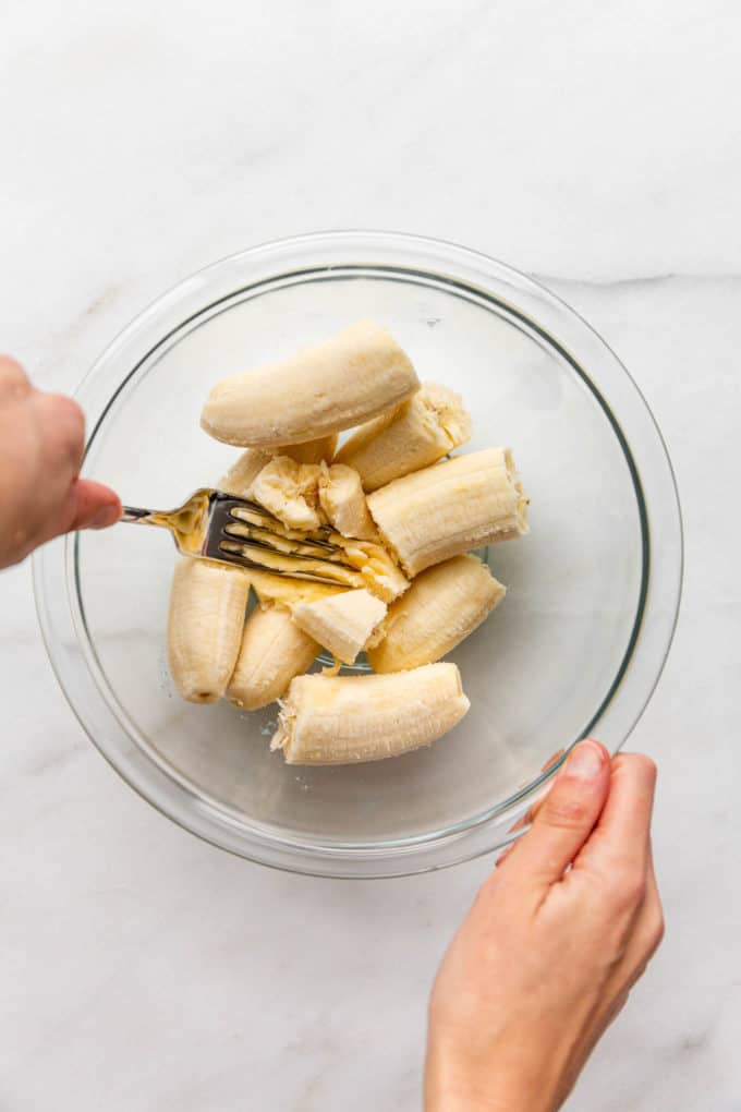 A hand mashing bananas with a fork