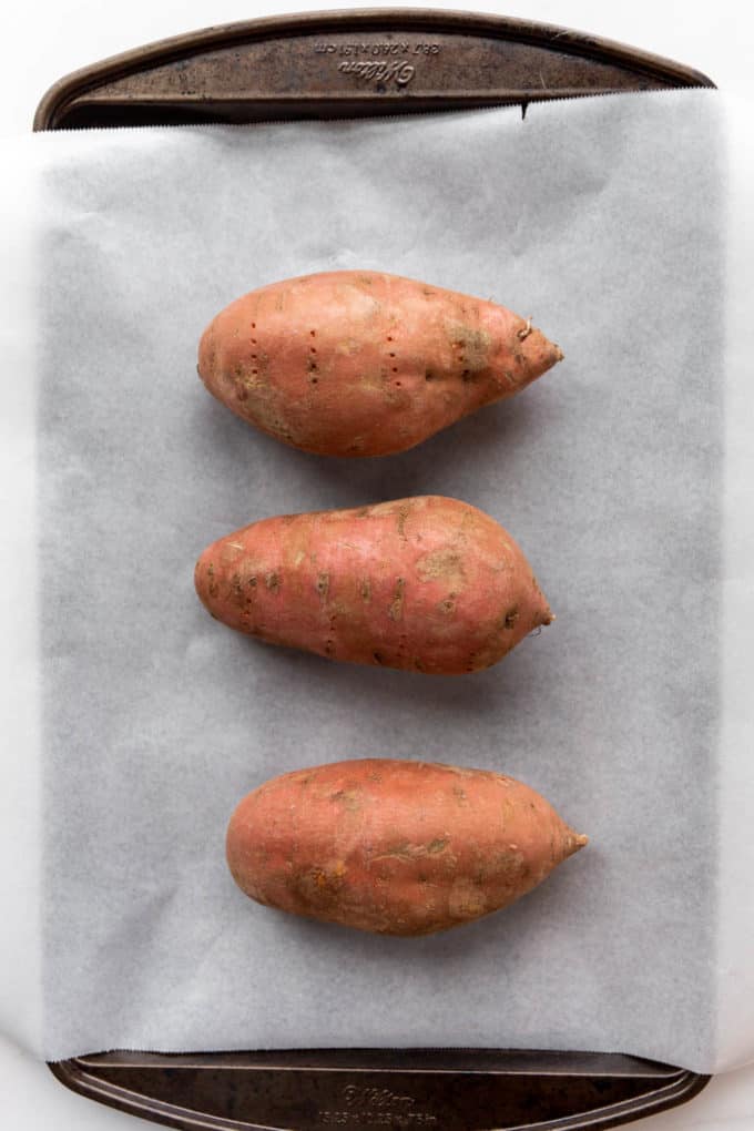 three unbaked sweet potatoes on a baking sheet