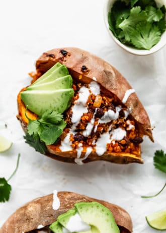 A black bean and quinoa stuffed sweet potato with sour cream and avocado on it
