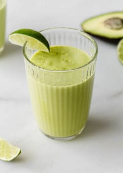 An avocado mango smoothie in a glass with a lime wedge