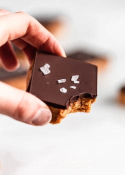 a hand holding a peanut butter protein bar topped with chocolate and salt