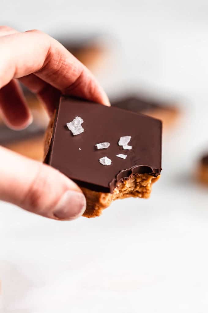 a hand holding a peanut butter protein bar topped with chocolate and salt