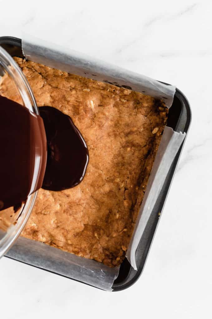 melted dark chocolate being poured into a pan of protein bars