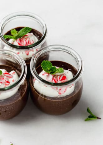three jars of mint chocolate pudding topped with whipped cream and crushed candy canes