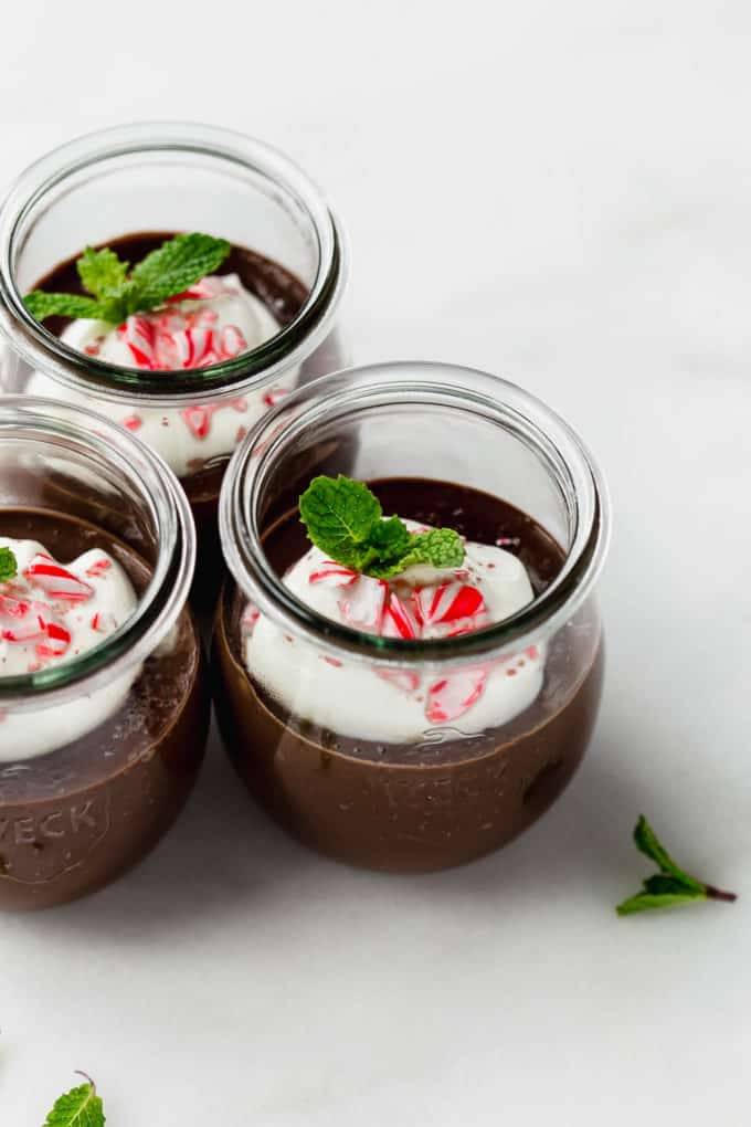 three jars of mint chocolate pudding topped with whipped cream and crushed candy canes