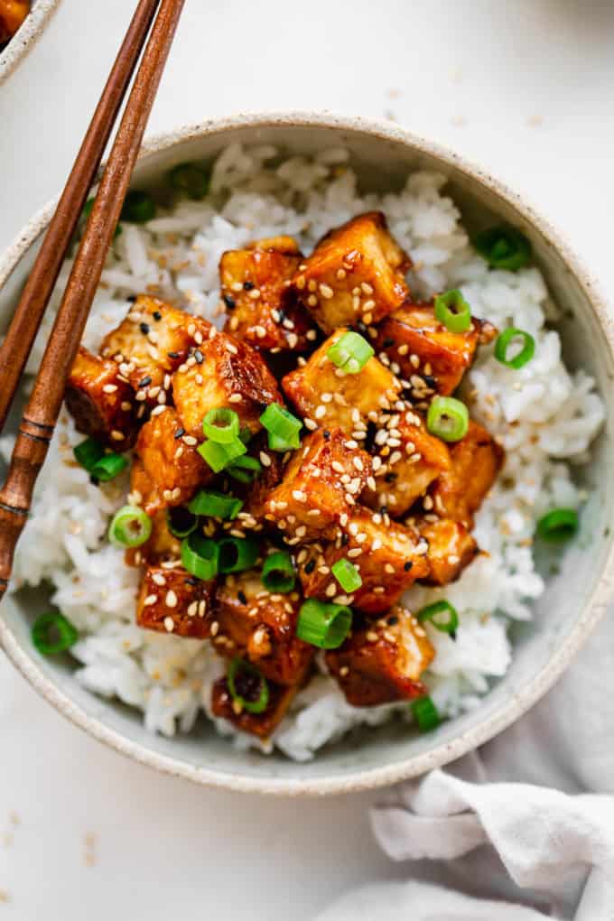 a bowl of sesame tofu on rice topped with chopped scallions