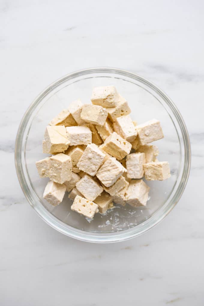cubed tofu tossed in cornstarch in a clear mixing bowl