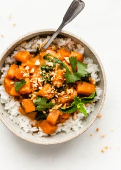 a bowl of sweet potato curry on rice topped with cilantro and mint