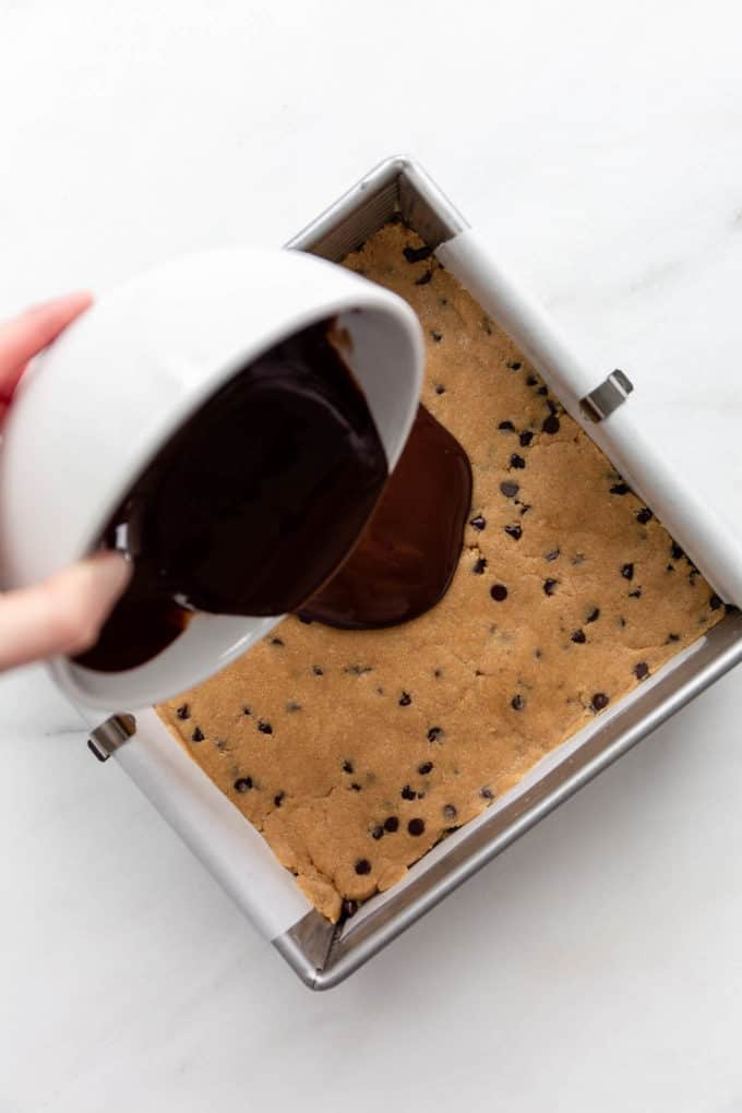 a bowl of chocolate being poured onto cookie dough bars