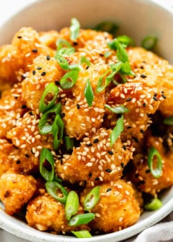 orange cauliflower topped with sesame seeds and scallions
