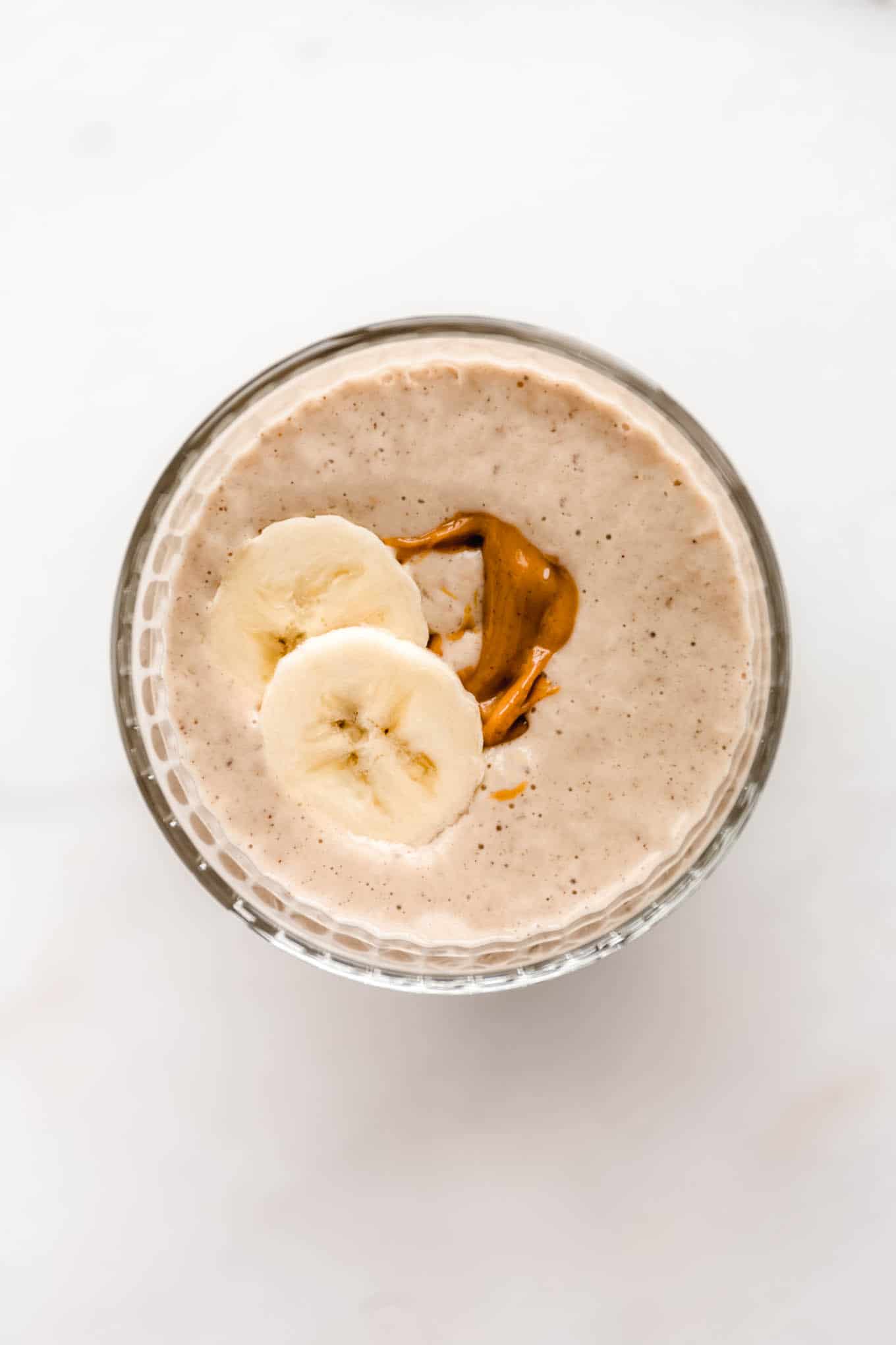 a top down view of a banana peanut butter smoothie with sliced banana on top