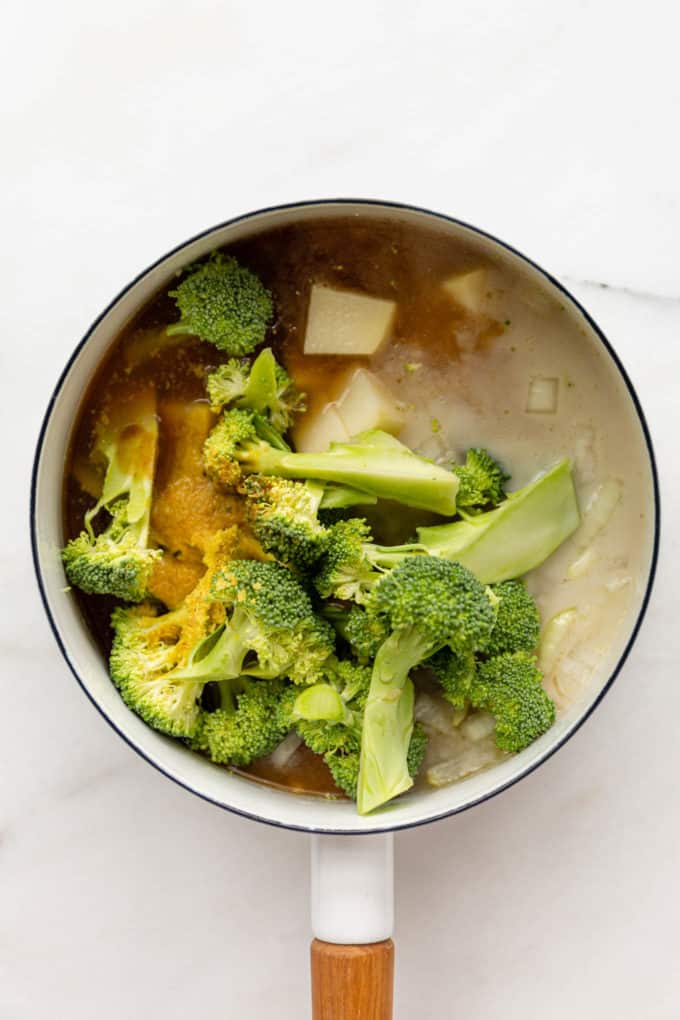 broccoli florets, potatoes, coconut milk and broth in a white pot