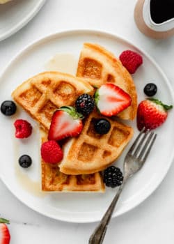 Almond flour waffles on a plate with maple syrup on the side