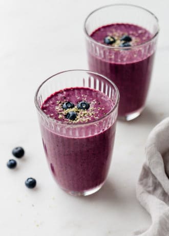 Two glasses of blueberry spinach smoothie topped with hemp seeds and blueberries