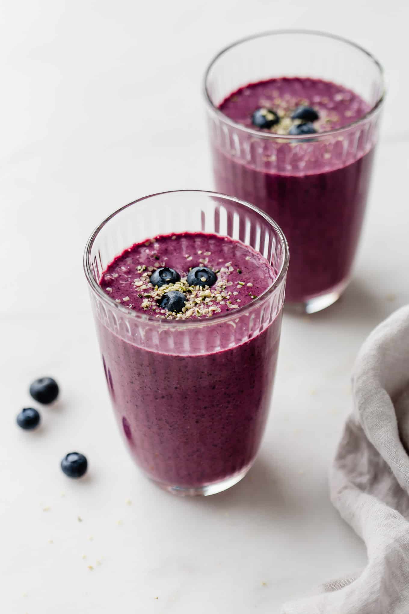 Two glasses of blueberry spinach smoothie topped with hemp seeds and blueberries