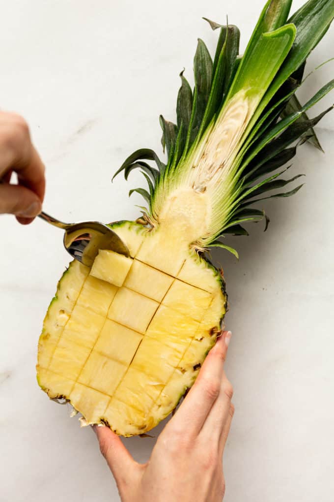 a spoon scoop out pineapple fruit from the skin