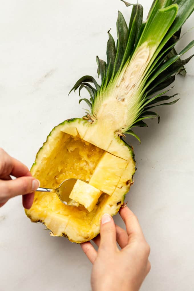 scooping out pineapple from the skin with a spoon