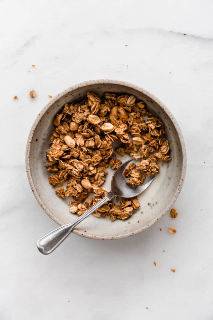 peanut butter granola in a bowl with a spoon on a marble counter
