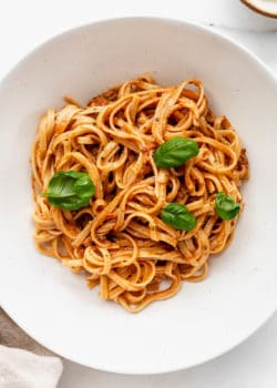 a bowl of red pesto pasta topped with basil leaves