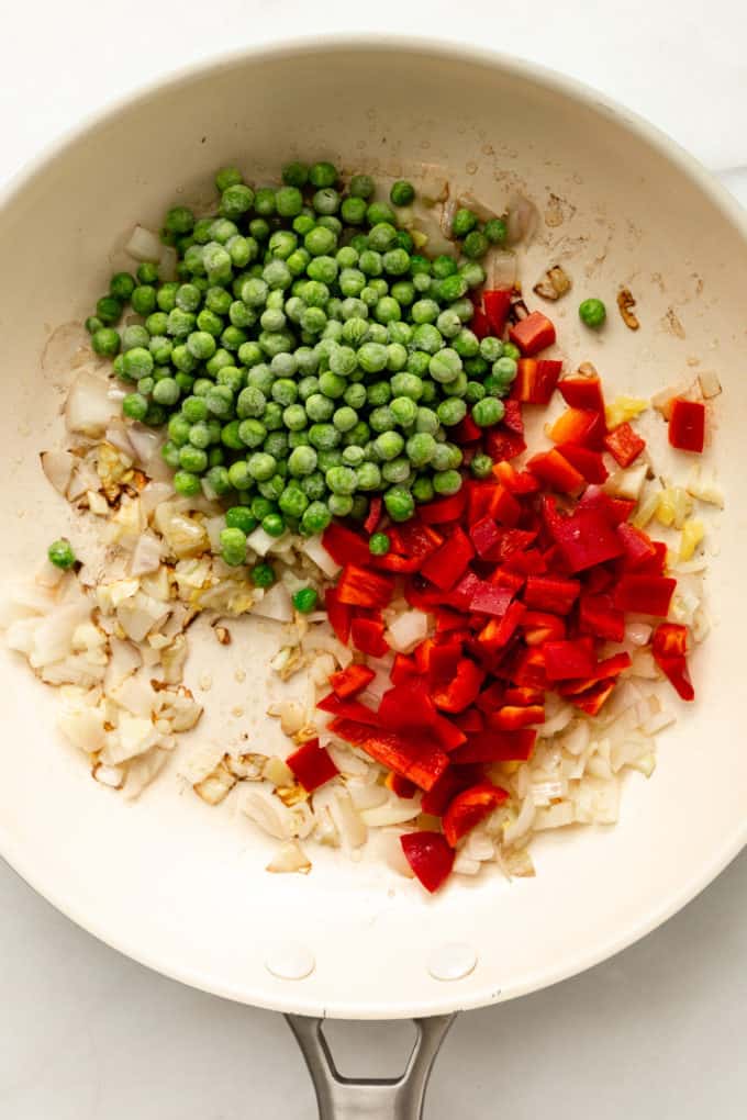 A white pan with onions, red peppers and peas in it