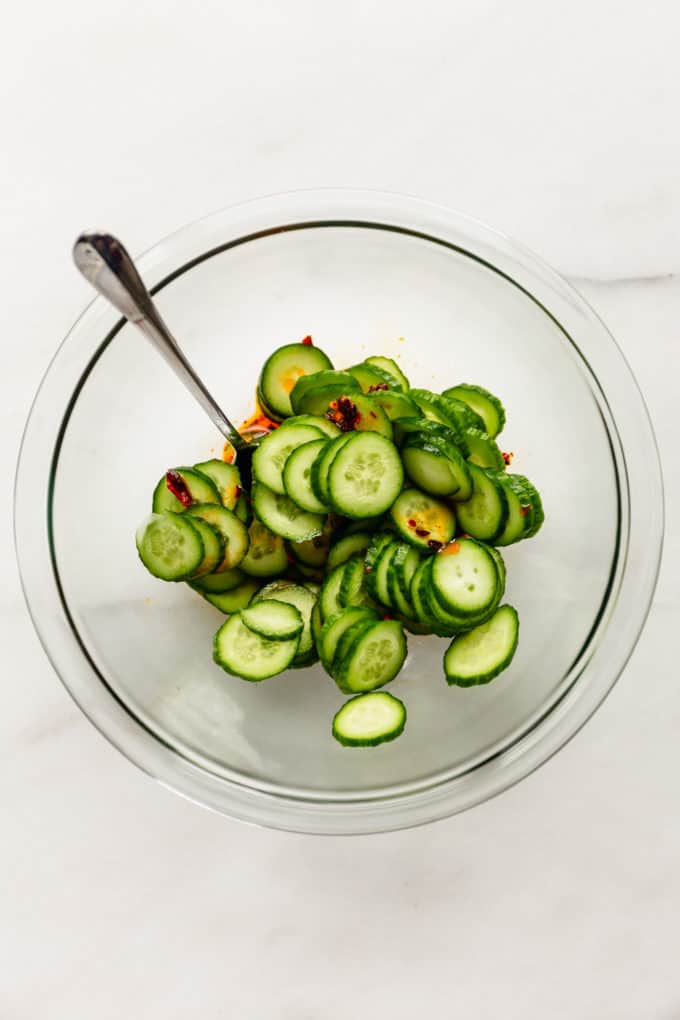 sliced cucumbers in a mixing bowl with dressing on the bottom