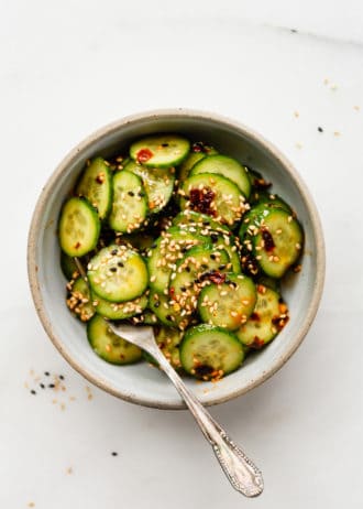 sliced cucumbers in a bowl topped with asian dressing and sesame seeds