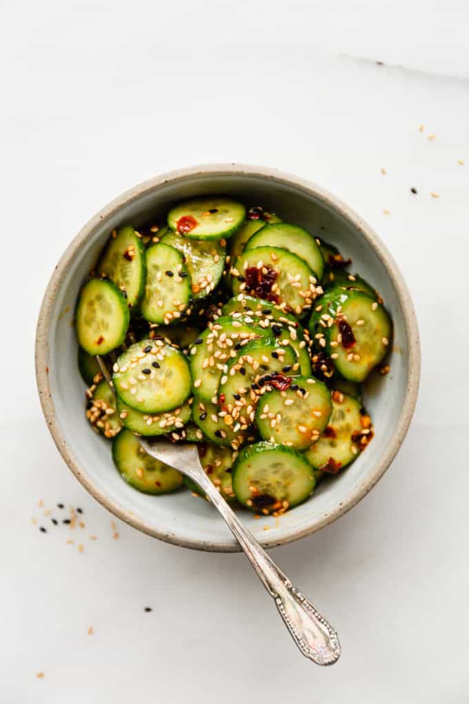 sliced cucumbers in a bowl topped with asian dressing and sesame seeds