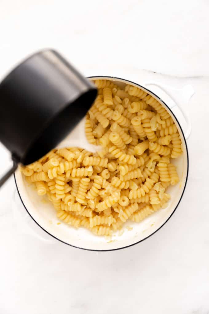 a measuring cup pouring pasta water into a pot of pasta