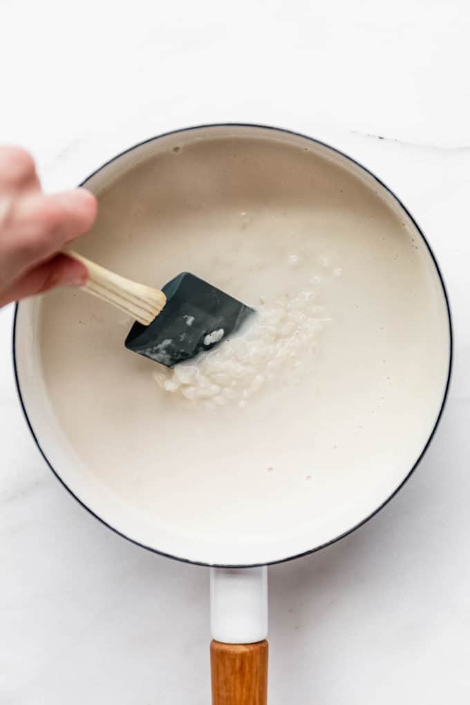 a spatula mixing rice in a pot of coconut milk