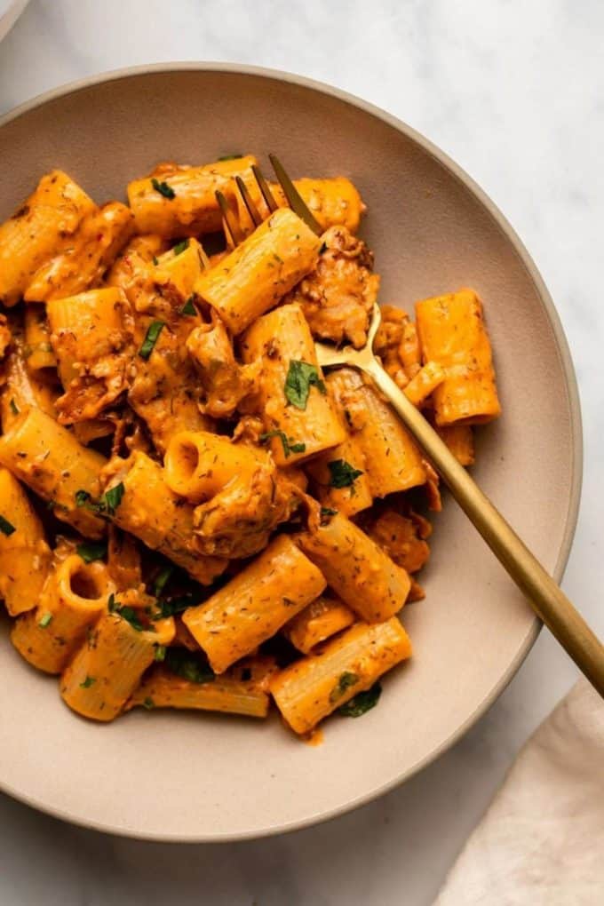 Rigatoni in a creamy red sauce on a pink plate with a gold fork
