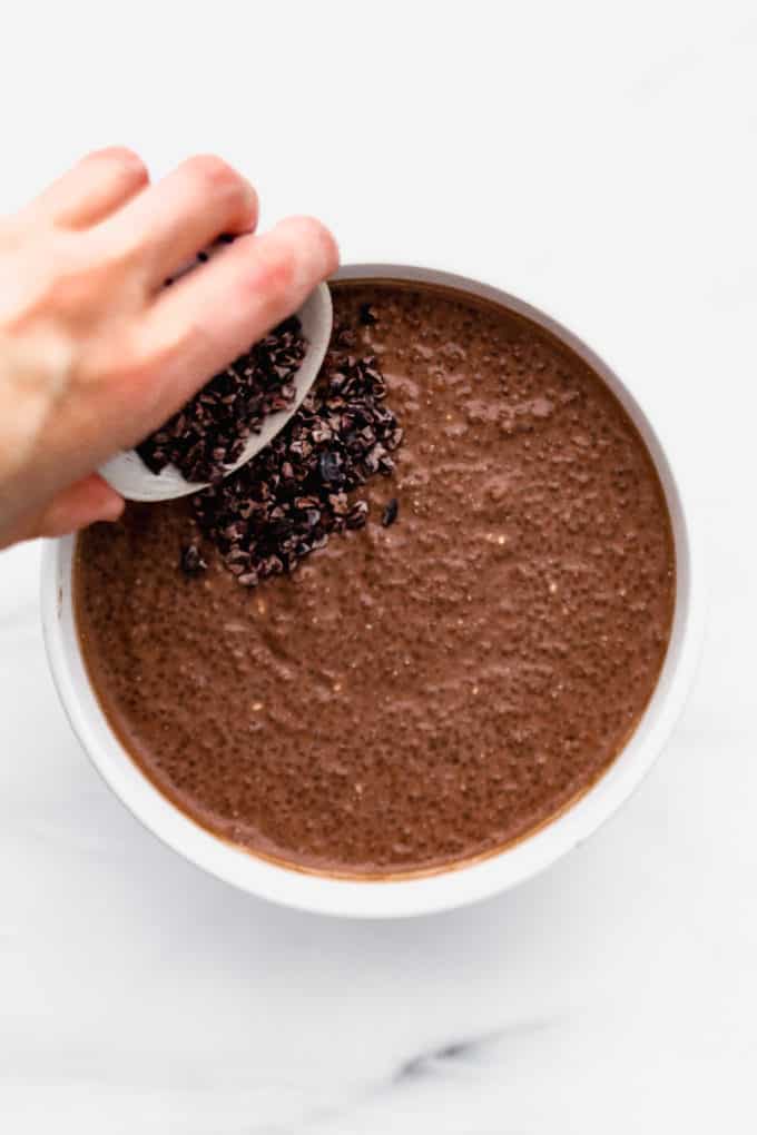 pouring cacao nibs into a bowl of chocolate chia pudding