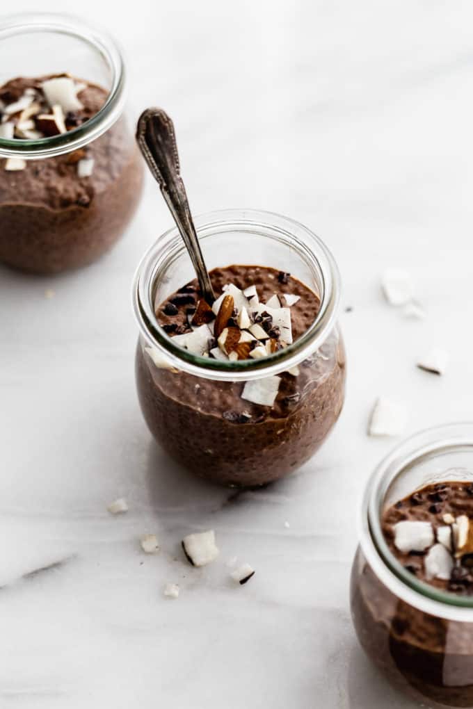 three cups of chocolate chia pudding topped with coconut and almonds