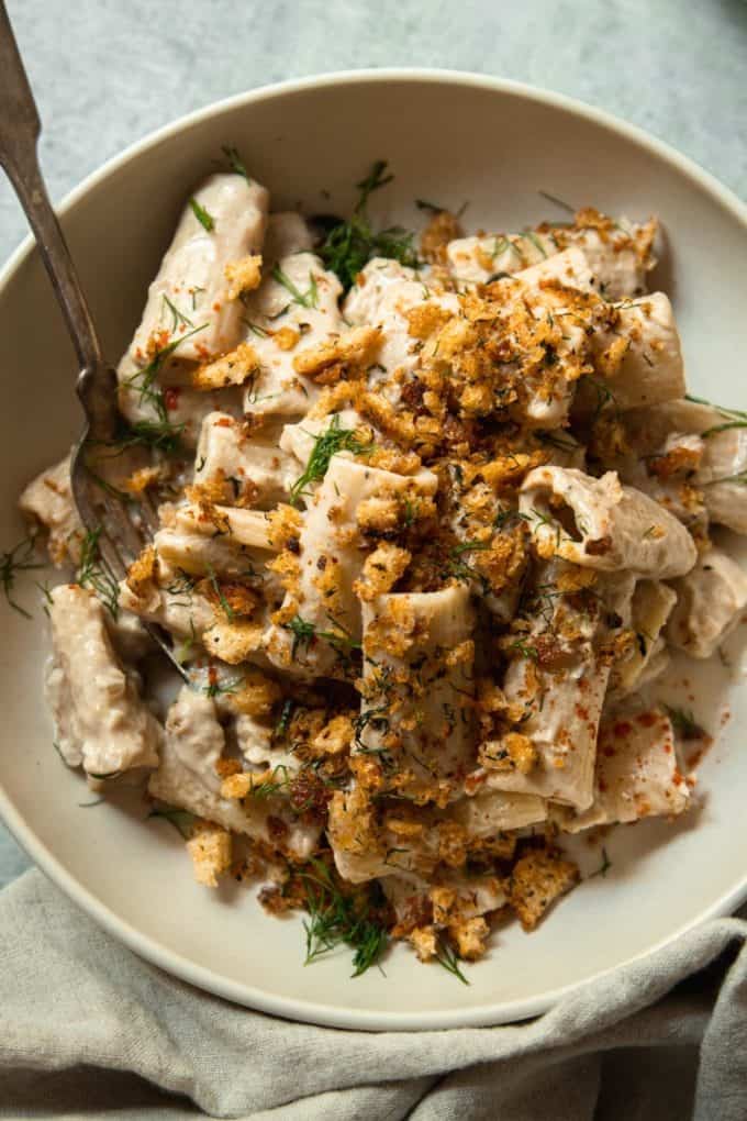 rigatoni in a creamy sauce topped with breadcrumbs in a beige bowl