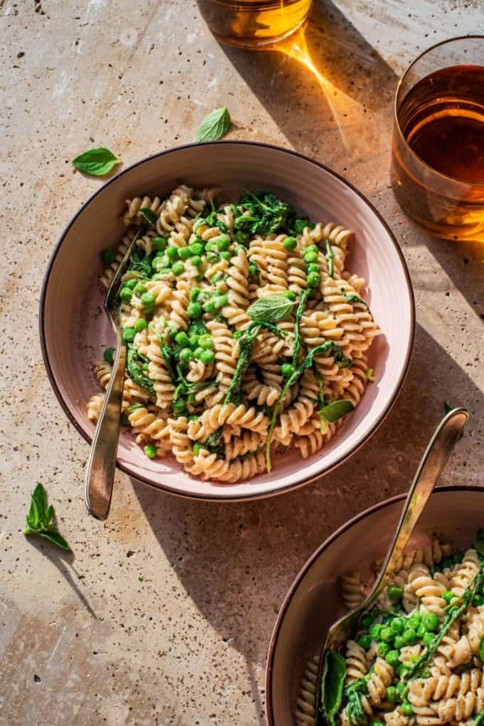 two bowls of fusilli pasta with green peas and basil
