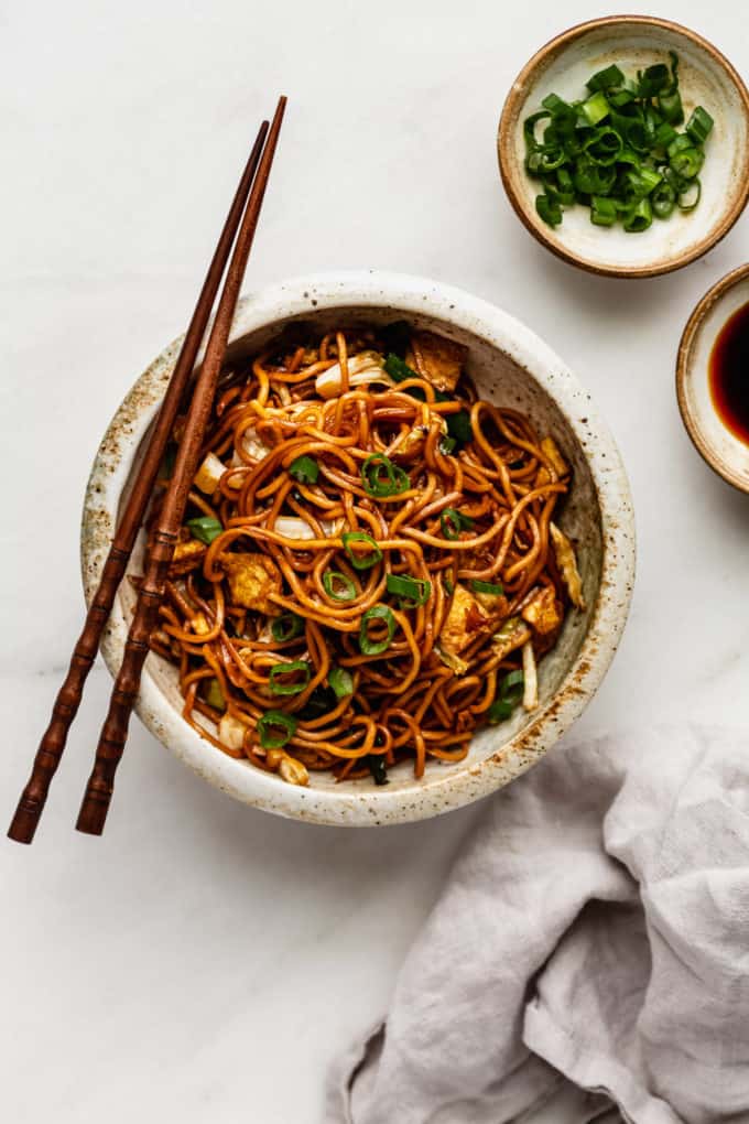 Mie goreng noodles in a bowl with a grey napkin and a small bowl of green onions on the side